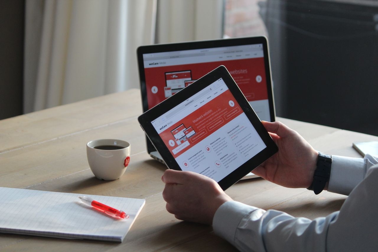 about-us-01 Business professional using a tablet and laptop with a hot drink, focusing on digital content review.